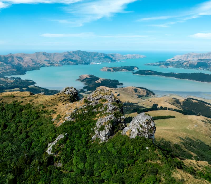 Aerial view of jagged rock outcrops on the Port Hills overlooking the turquoise Lyttelton Harbour.
