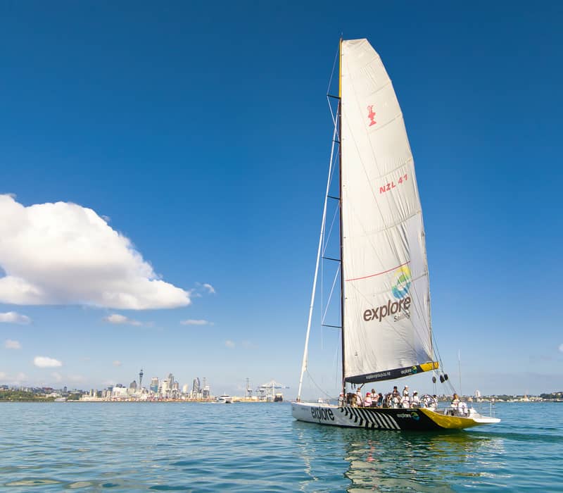 Sailboat with people sailing on water near a city skyline on a clear day.
