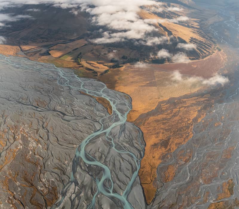 Aerial view of a glacial river flowing through a mountainous valley with clouds above.