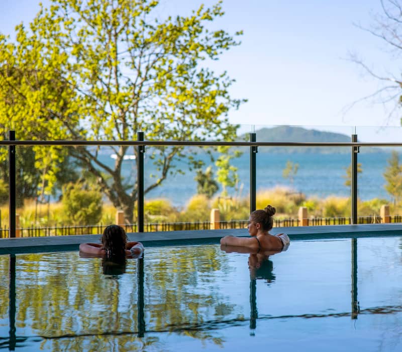 People bathing in pools at Wai Ariki spa and enjoying view of lake.