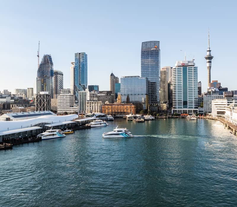Auckland city skyline and waterfront with a Fullers ferry on the harbour under a clear blue sky.