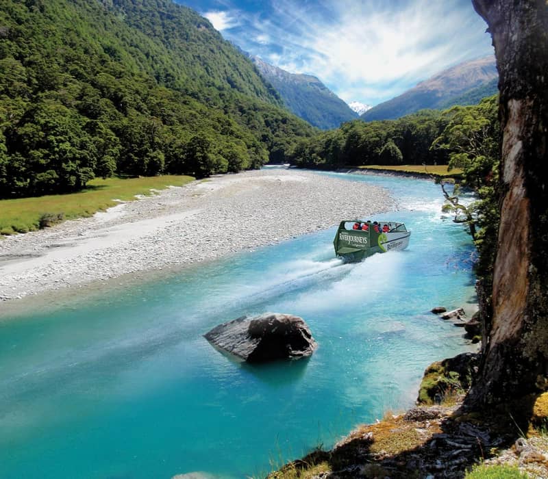Jet boat speeding along a clear blue river with forested mountains in the background.