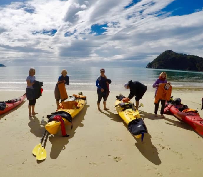 People prepping kayaks on sandy beach with calm sea and cloudy sky.