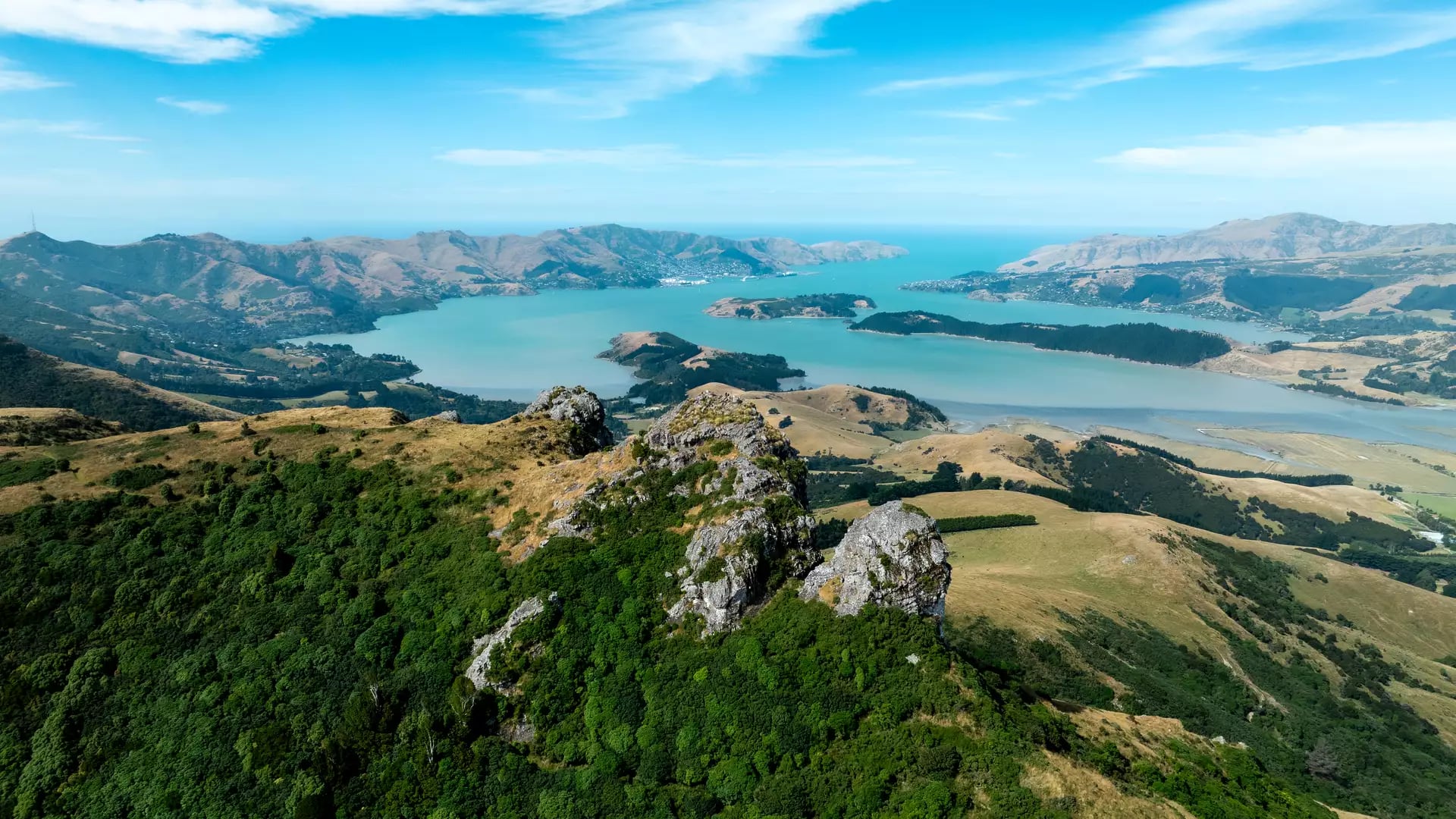 Aerial view of jagged rock outcrops on the Port Hills overlooking the turquoise Lyttelton Harbour.