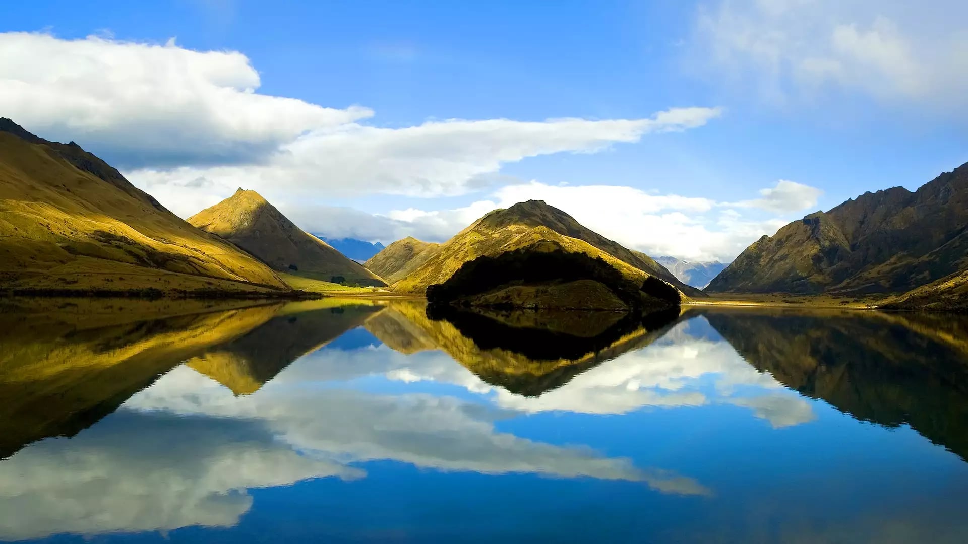 Calm lake reflecting mountains and clouds under blue sky
