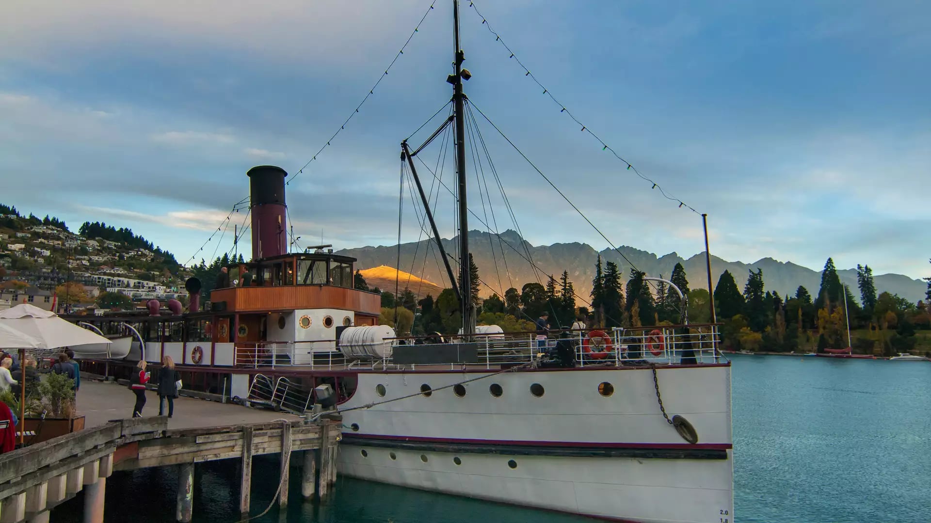 Steamship docked at a pier with mountains and water in the background during sunset.
