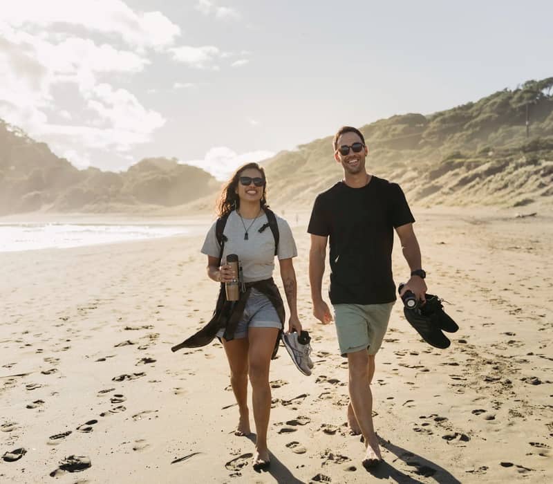 Couple walking barefoot along sandy beach in Auckland