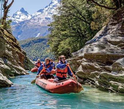 Group of people rafting on a clear river with mountains and forest in the background
