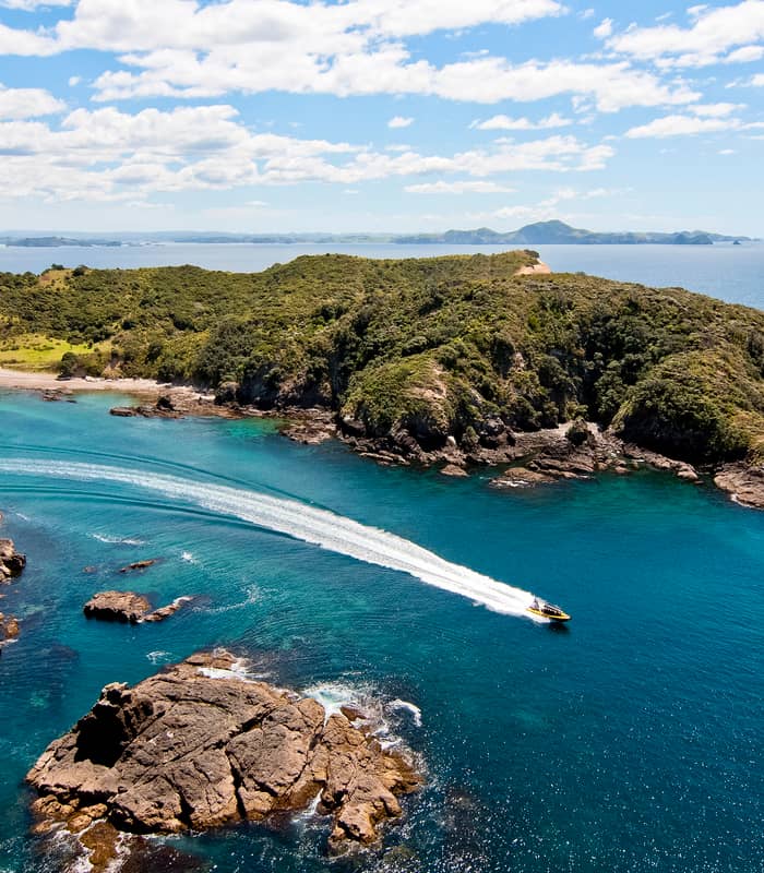 Explore speedboat travelling through blue water between islands in the Bay of Islands.