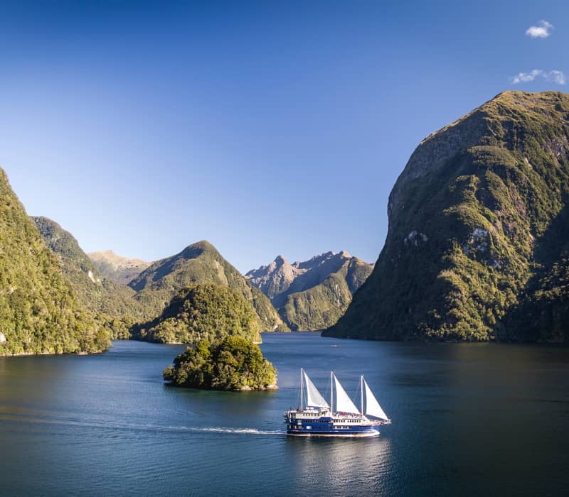 Cruise boat sailing in forested fjord with mountains and clear blue sky