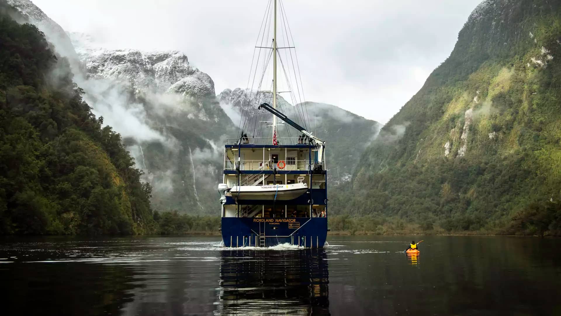 Cruise ship in fjord surrounded by foggy mountains and kayak on calm water