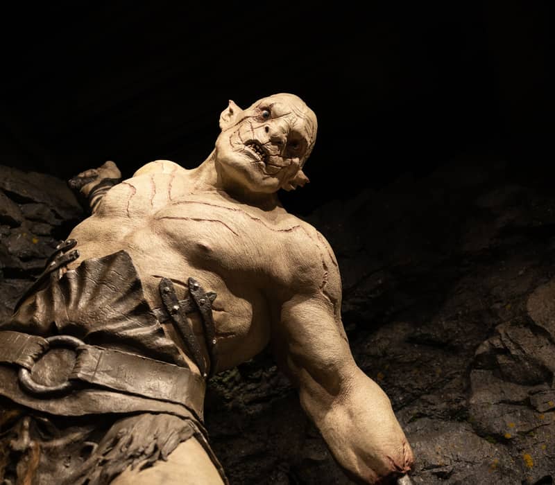 Muscular troll statue with scars and belt in a rocky cave environment.