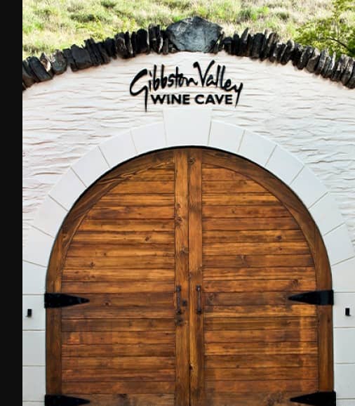Wooden arched door entrance to Gibbston Valley Wine Cave with signage and green roof