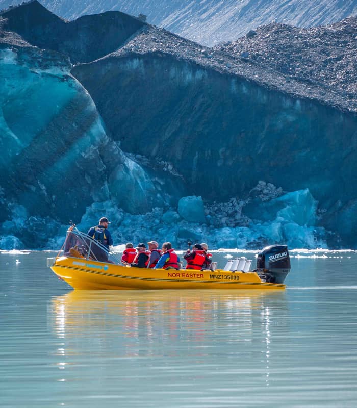 Group of tourists in yellow boat touring near a blue glacier with rocky mountain background.