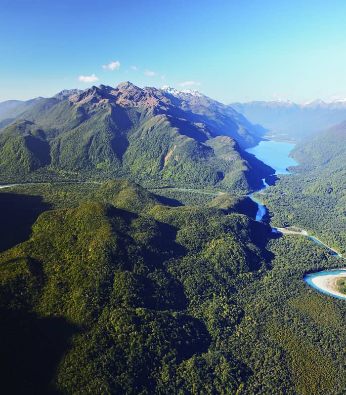 Aerial view of a valley with a winding river, forest, lakes, and mountains under a clear blue sky.