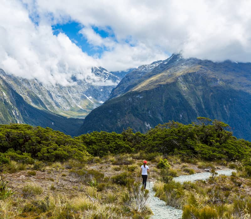 Hiker walking on a trail with mountains and clouds in the background