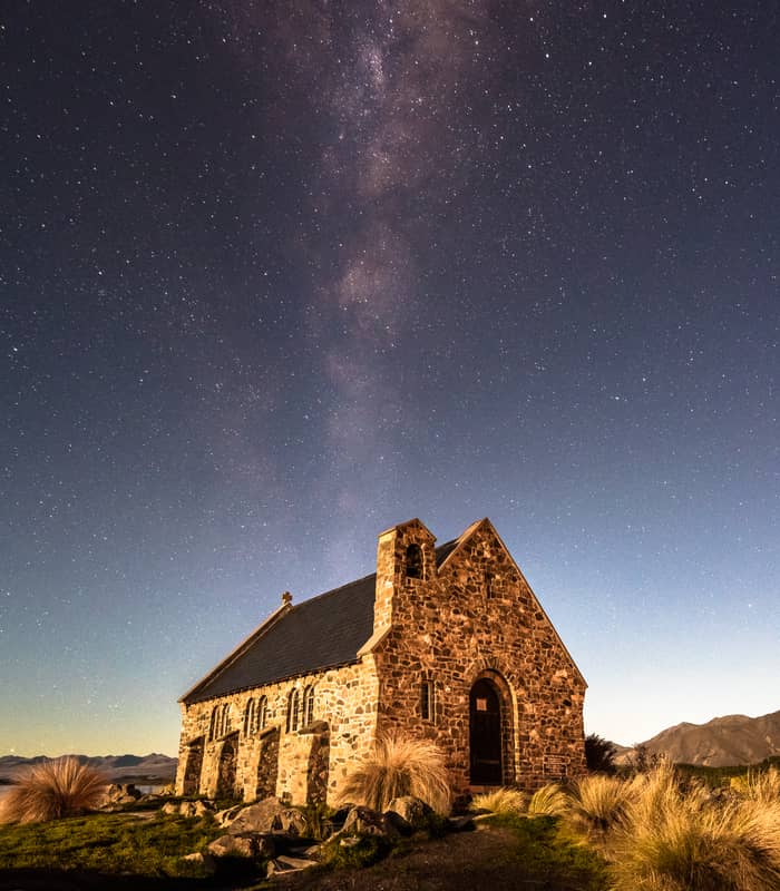 Stone church by lake with starry night sky and Milky Way above.